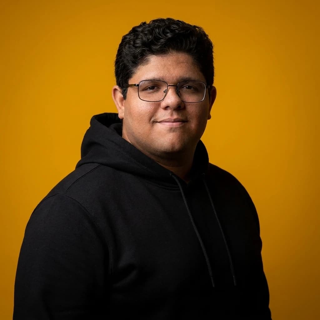 Mathews Laragnoit (Thews) de óculos e moletom preto, sorrindo, sobre fundo âmbar